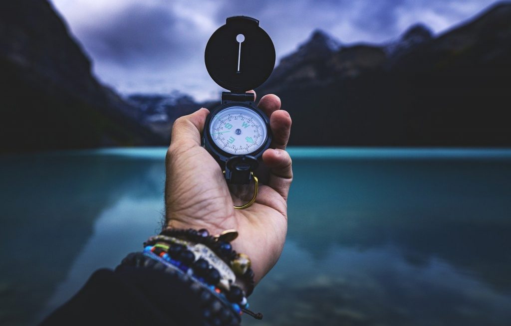 An extended hand holding a compass overlooking water